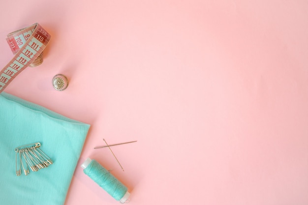 Sewing accessories, turquoise fabric on pink background. Fabric, pins, threads and needles.