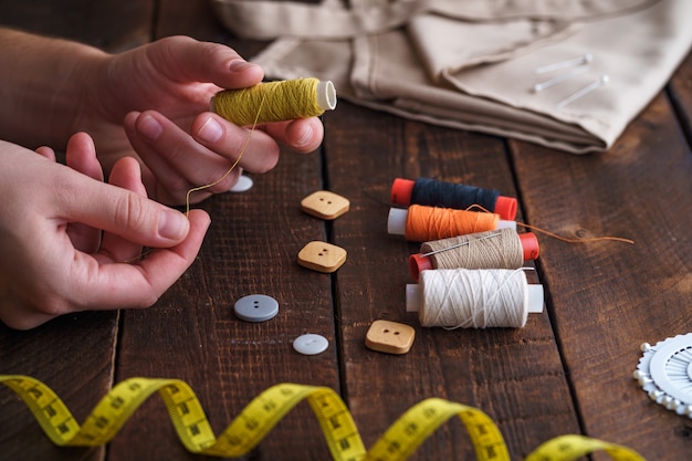 Sewing kit for needlework on wooden surface. Spool of thread in the hands of a seamstress