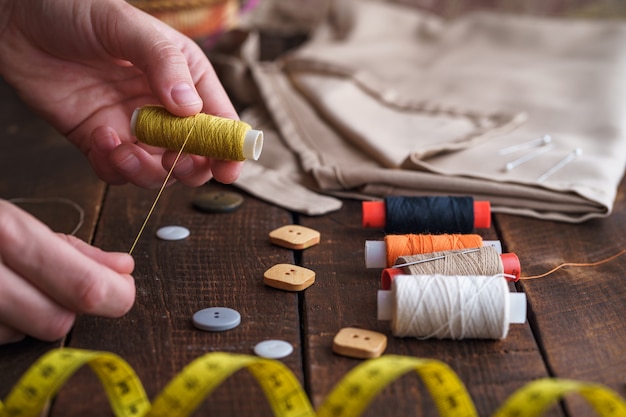 Швейный набор для пошива на деревянной поверхности. Катушка ниток в руках портнихи