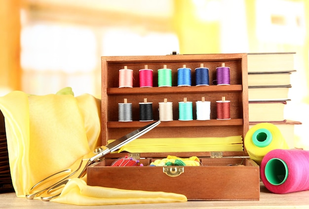 Sewing kit in wooden box with books and cloth table on bright background