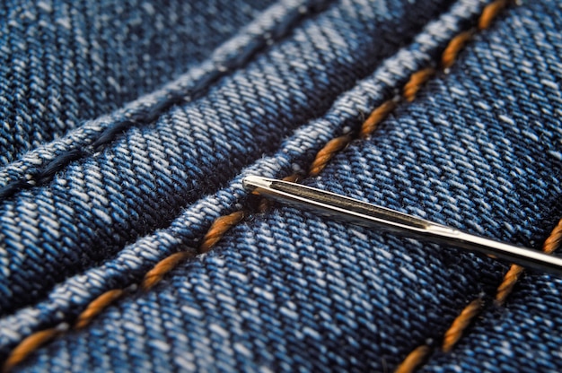 Швейная игла ложится на шов джинсовой ткани синего цвета. крупный план.