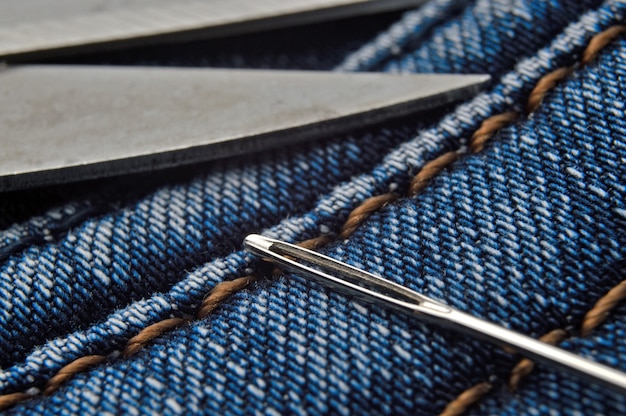 Photo sewing needle and scissors lie on blue jeans