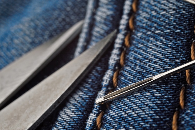 Sewing needle and scissors lie on blue jeans