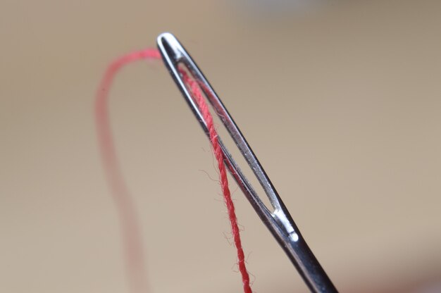 針の目を通して赤い糸が付いているミシン針。大きい。