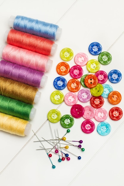 Sewing pins threads and colored buttons on a white table