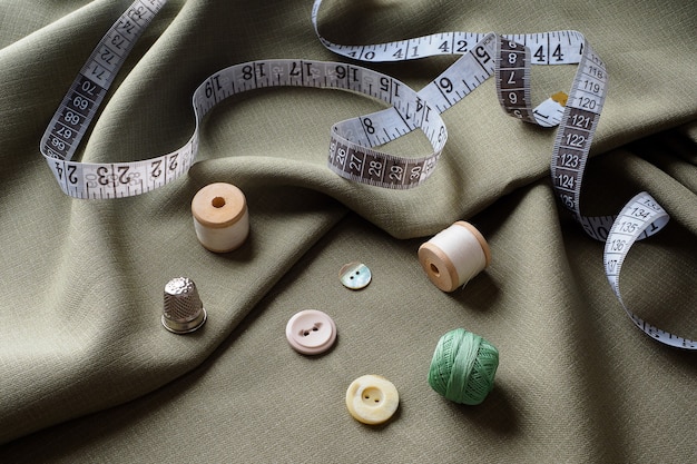 Sewing supplies lie on draped fabric, close-up. Sewing background. Spools of thread, a centimeter, scissors, a thimble, on a gray draped cloth. Atelier concept. Fashion designer. Sewing composition.