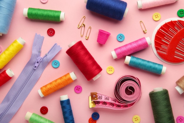 Sewing supplies on pink background sewing thread scissors a large spool of thread pieces of cloth needlescentimeter buttons