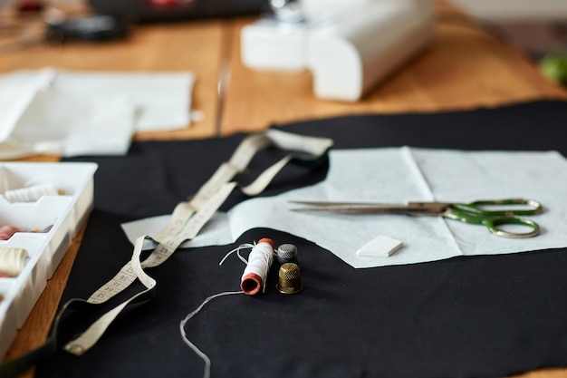 Sewing supplies on a wooden table: sewing thread, scissors, pieces of cloth, needles, centimeter, pattern.