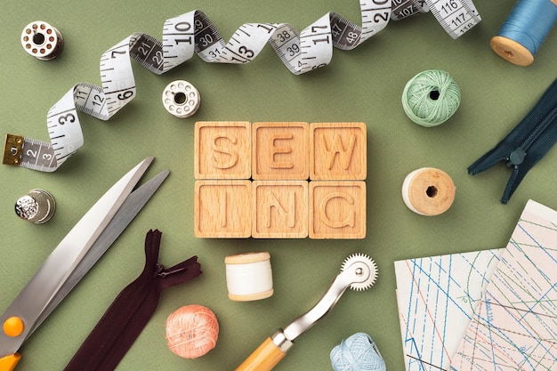 裁縫道具はさみ針糸センチ紙パターンフラットレイアウト「裁縫」という言葉は木製の立方体からレイアウトされています明るい裁縫の背景コンセプトデザイナーワークスペース