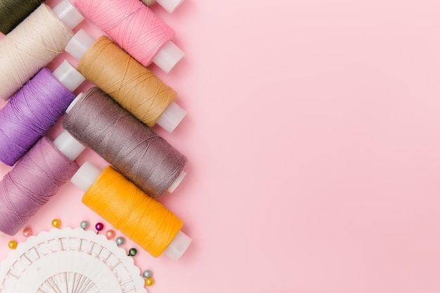 エレガントなピンクの背景に縫製ツールとミシンアクセサリードレスメイキングテーラーバックグラウンドマルチカラーミシン糸スレッドスプールニードルピントップビューフラットレイテーラーのビジネスのために