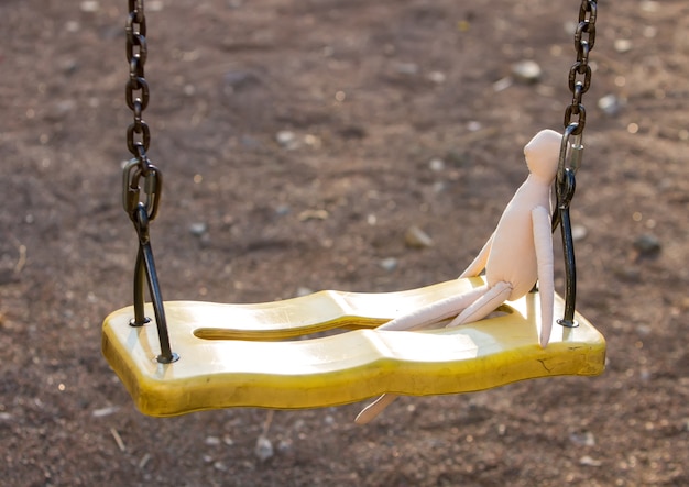 A sewn faceless doll in profile sits on a swing leaning on a chain.