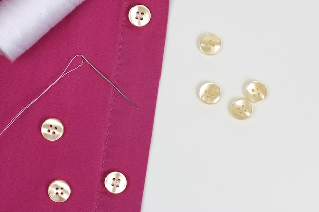 シャツに白い糸の真珠のボタンが付いた針で縫い付けられています