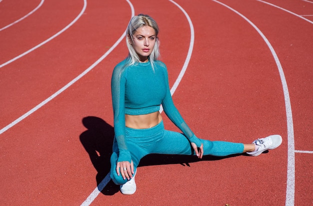 Sexual athletic woman in fitness costume stretching on running track sport