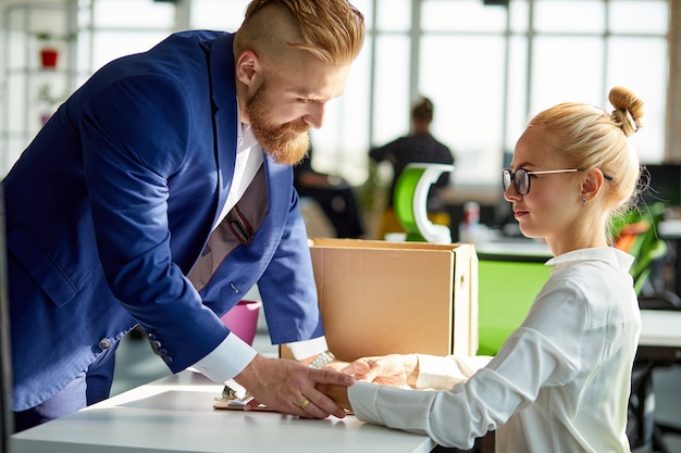 Sexual harassment in business office by bearded boss, blonde female sits at work place