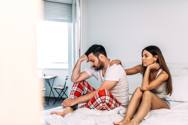 Photo sexual problems concept. upset man sitting on the bed with woman comforting him.