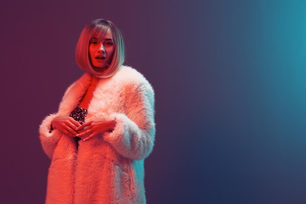 Sexy adorable blonde woman in fluffy fur coat sparkly dress\
fold hands open mouth posing isolated in blue turquoise red color\
light studio background neon party fashion concept copy space\
banner