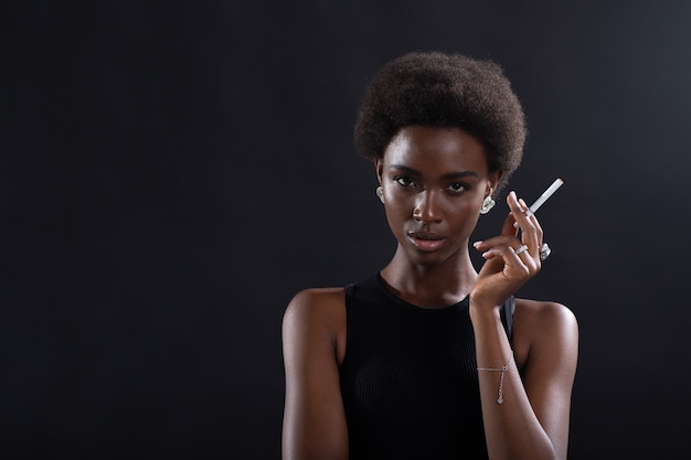 Sexy african american woman smoking cigarette on black background