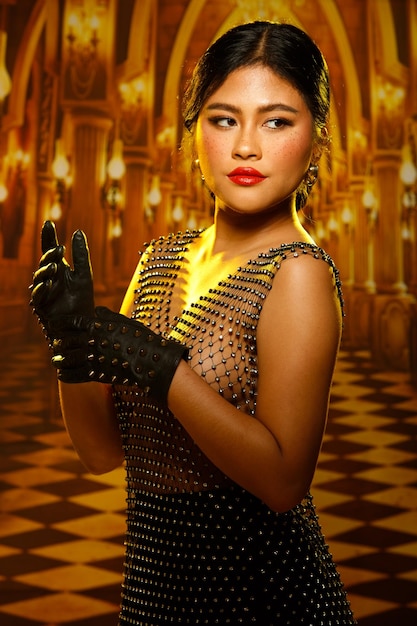 Sexy Asian 20s woman with beautiful freckles face and chubby body wear crystal sensual sparkle dress over gold yellow light in Palace mansion for private party studio lighting