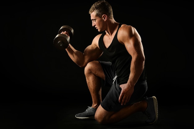 Sexy athlete with dumbbell on black background