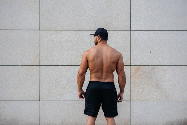 Sexy atleet staat met zijn rug tegen de muur. Fitness. Gezonde levensstijl.