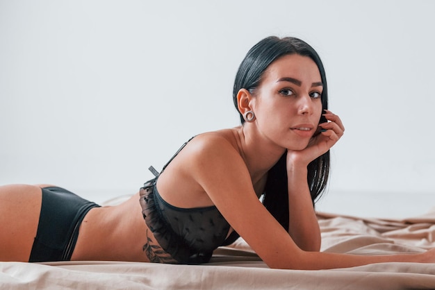 Сексуальная привлекательная брюнетка в черном интимном белье и с татуировками на теле лежит на полу.
