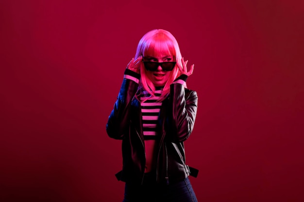 Sexy attractive woman with leather jacket and sunglasses feeling stylish in dark fluorescent light background. Confident person with funky style and perfect fashion posing on camera.