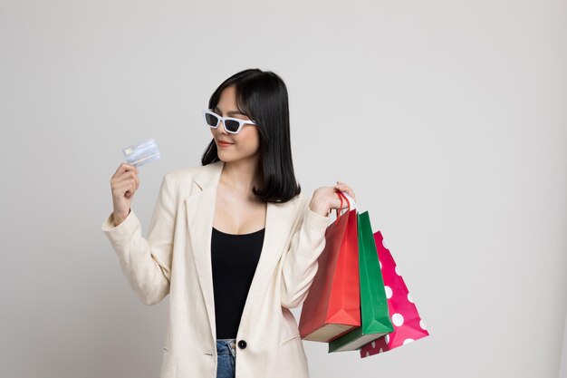 Sexy beautiful asian girl holding shopping bag and credits card mockup on isolated white background. She wearing fashion sunglasses.