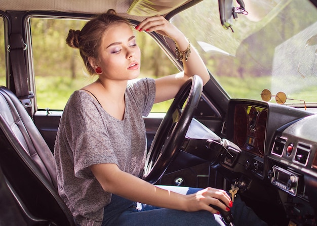 Sexy beautiful young woman sitting in the car with his hand on a retro wheel