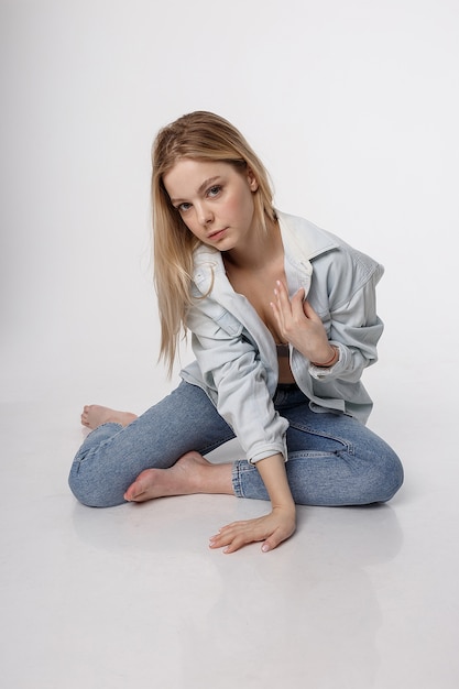 Foto sexy blanke vrouw met lang haar poseren in blauw shirt en spijkerbroek op witte studio