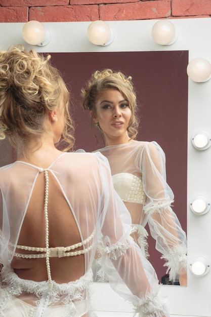 Sexy blond in white tulle dress looking at the mirror High quality photo