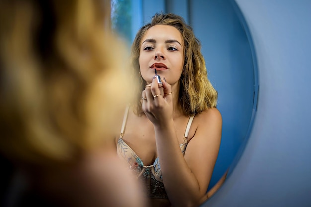 Sexy blonde vrouw die make-up doet voor de spiegel.