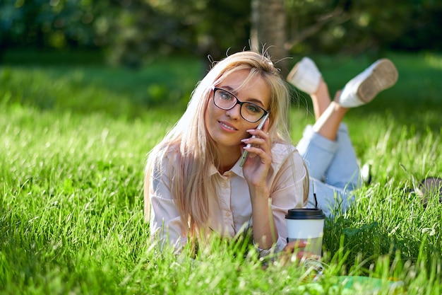 Sexy blonde vrouw praten op de mobiele telefoon en liggend op de weide.