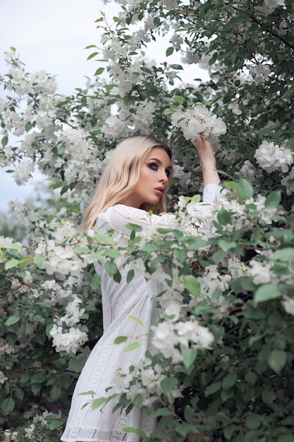 リンゴの木の枝で夏のセクシーなブロンドの女性。白いリンゴの花の女の子の肖像画