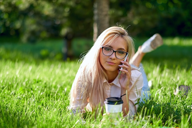 携帯電話で話し、牧草地に横たわっているセクシーなブロンドの女性。