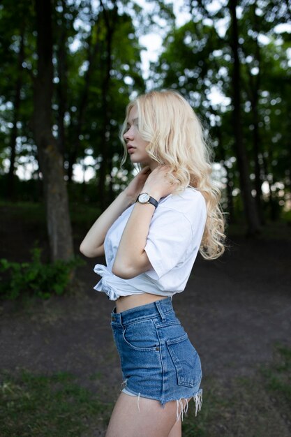 Sexy blonde woman with closed eyes, touching her neck, dressed in a denim shorts and white top, posing in profile,