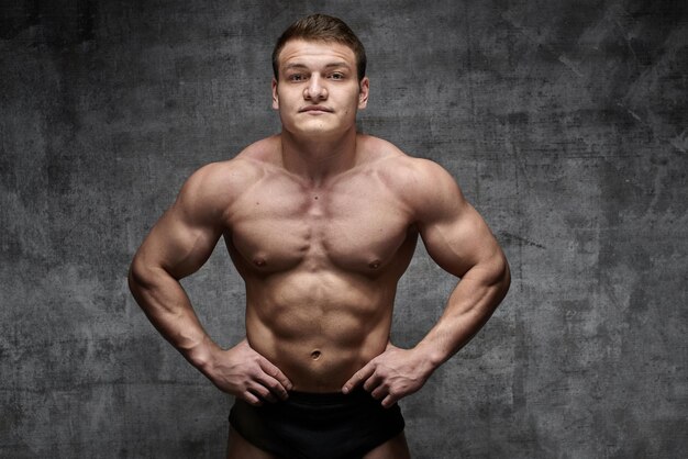 Sexy bodybuilder man posing on dark background in black shorts. Handsome pumped male body isolated with free space for advertising