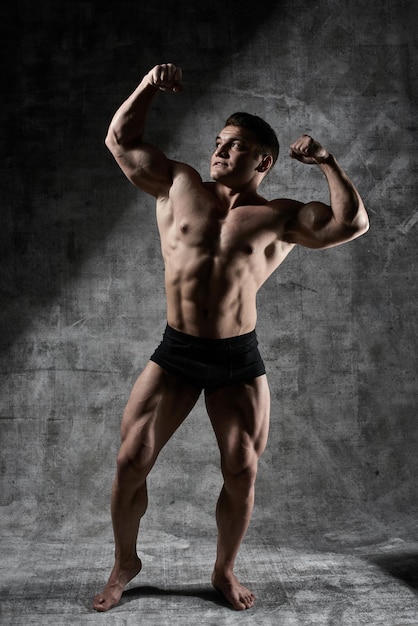 Photo sexy bodybuilder man posing in full growth on dark background in black shorts. handsome pumped male body isolated with free space for advertising