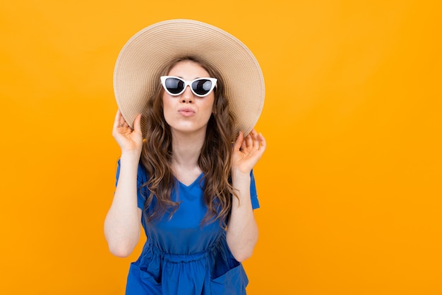 Sexy bruinharige vrouw in een hoed en bril op een gele ondergrond