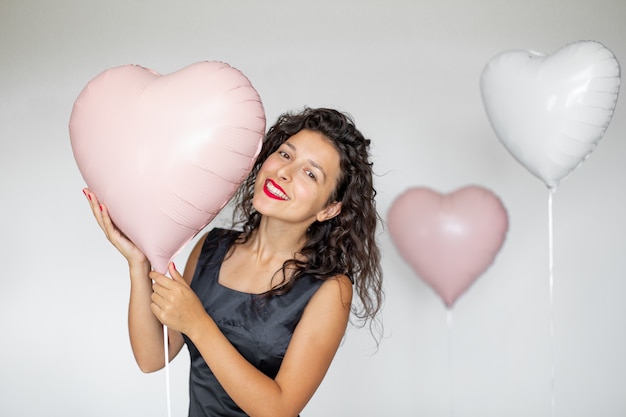Сексуальная брюнетка девушка позирует с воздушными шарами в форме сердца на белом фоне.