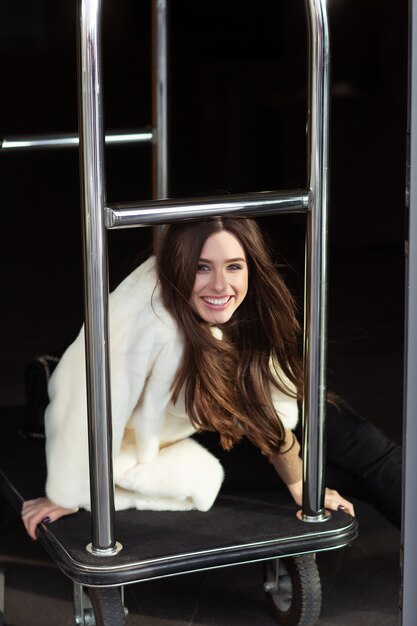 Sexy brunette girl standing near hotel luggage cart.