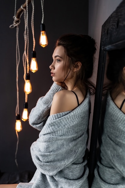 Sexy brunette girl wearing grey cardigan and lingerie near mirror