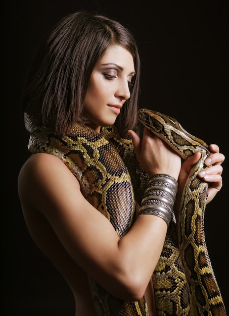 Sexy brunette holding python over black