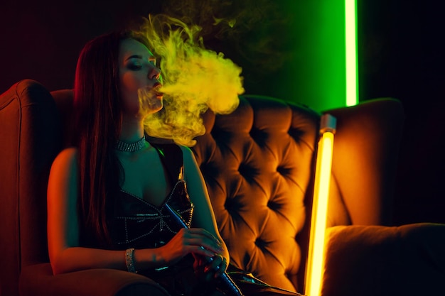 Sexy brunette model is smoking a hookah exhaling a smoke at a luxury night club.