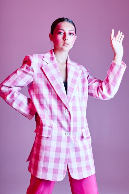 セクシーなブルネットの女性の高級服ファッション格子縞のブレザーピンクの背景は変更されていません