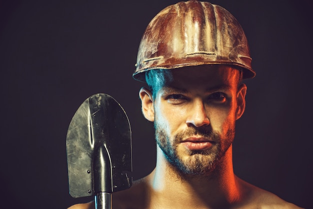 Sexy builder in protective helmet hold sapper shovel construction workmining concept repairman male