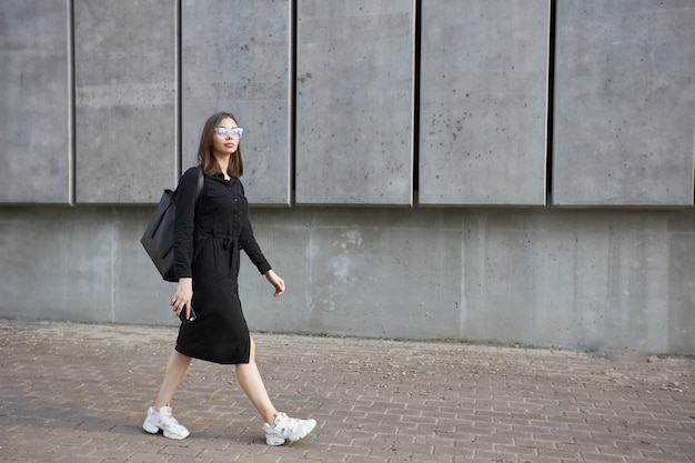 Сексуальная деловая брюнетка женщина с макияжем в черной одежде гуляет по цементным улицам города