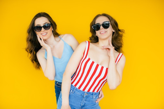 Sexy carefree women posing near yellow wall in sunglasses Positive models going