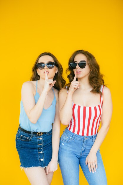 Sexy carefree women posing near yellow wall in sunglasses Positive models going