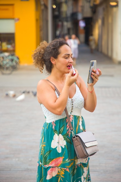 Sexy curlyhaired woman painting her lips on the street