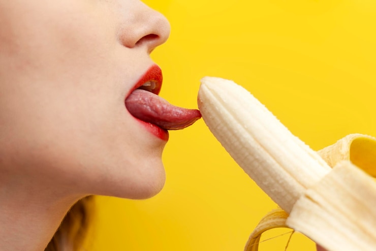 Foto sexy en intieme pijpbeurt concept vrouw likt en neemt banaan in haar mond op gele achtergrond
